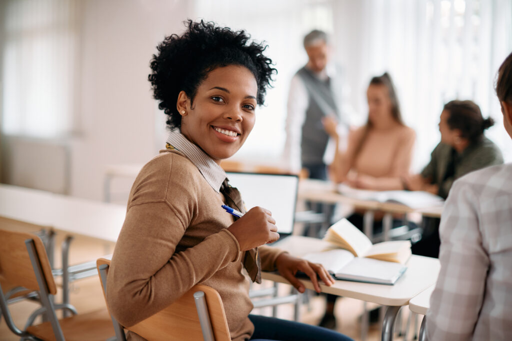 Happy black woman attends class at lecture hall and looks at camera.