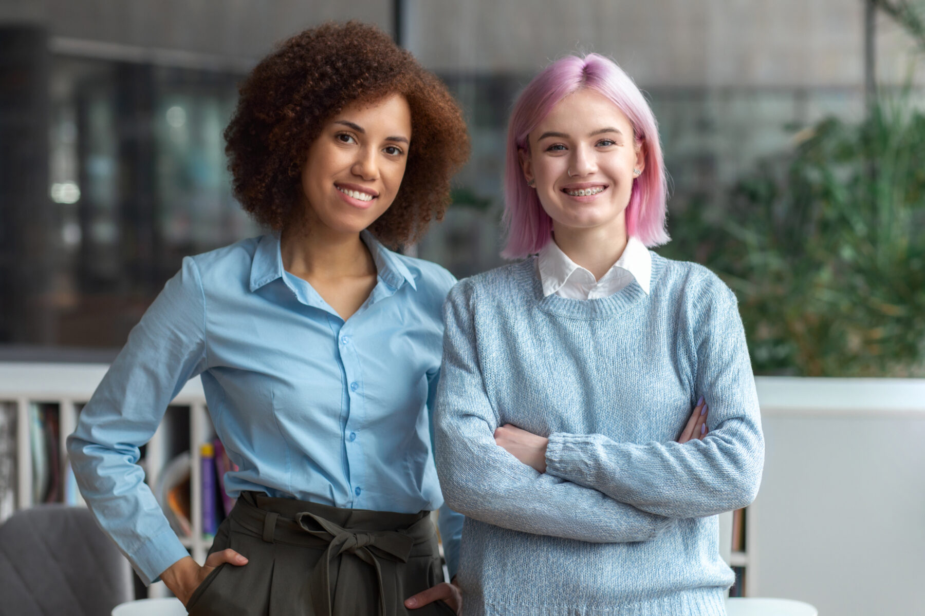 Two happy multiethnic modern young women entrepreneurs or colleagues standing in modern office looking at the camera and smiling, Business team